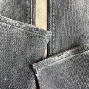 May include: Close-up of gray denim jeans, showing the details of the seams and distressed edges. The fabric has a textured appearance, with visible stitching and slight wear.