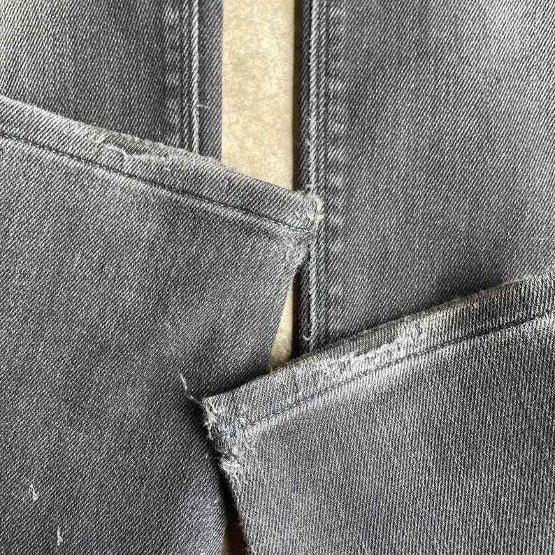 May include: Close-up of gray denim jeans, showing the details of the seams and distressed edges. The fabric has a textured appearance, with visible stitching and slight wear.