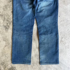 Op de afbeelding: Blauwe denim jeans met een rechte pijp. De jeans hebben een vervaagde wassing en zichtbare slijtplekken, wat wijst op een vintage of versleten uitstraling. De stof lijkt een mediumgewicht denim te zijn.