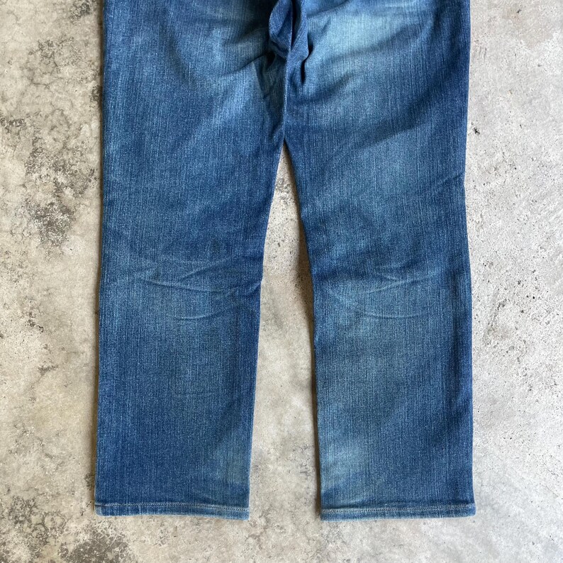 Op de afbeelding: Blauwe denim jeans met een rechte pijp. De jeans hebben een vervaagde wassing en zichtbare slijtplekken, wat wijst op een vintage of versleten uitstraling. De stof lijkt een mediumgewicht denim te zijn.