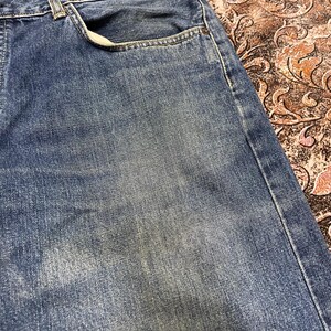 May include: A pair of blue denim jeans featuring a classic five-pocket construction with a faded wash effect. The fabric displays a textured weave with visible stitching along the seams and a standard waistband with a front pocket opening.