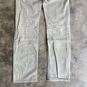 K&ouml;nnte beinhalten: Hellgraue Jeans aus Denim. Die Jeans hat einen geraden Beinverlauf und ein verwaschenes Aussehen. Der Stoff weist eine subtile Textur und Abnutzung auf. Die Jeans liegt flach auf einer neutralen Oberfl&auml;che.