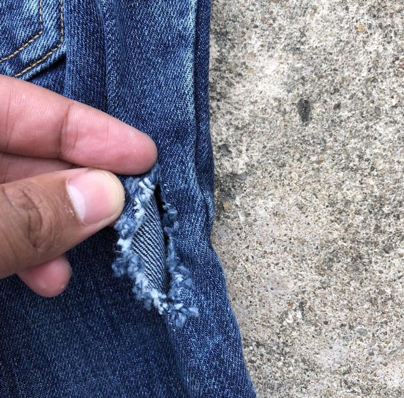 Op de afbeelding: Close-up van een paar blauwe spijkerbroeken met een klein gat in de stof.