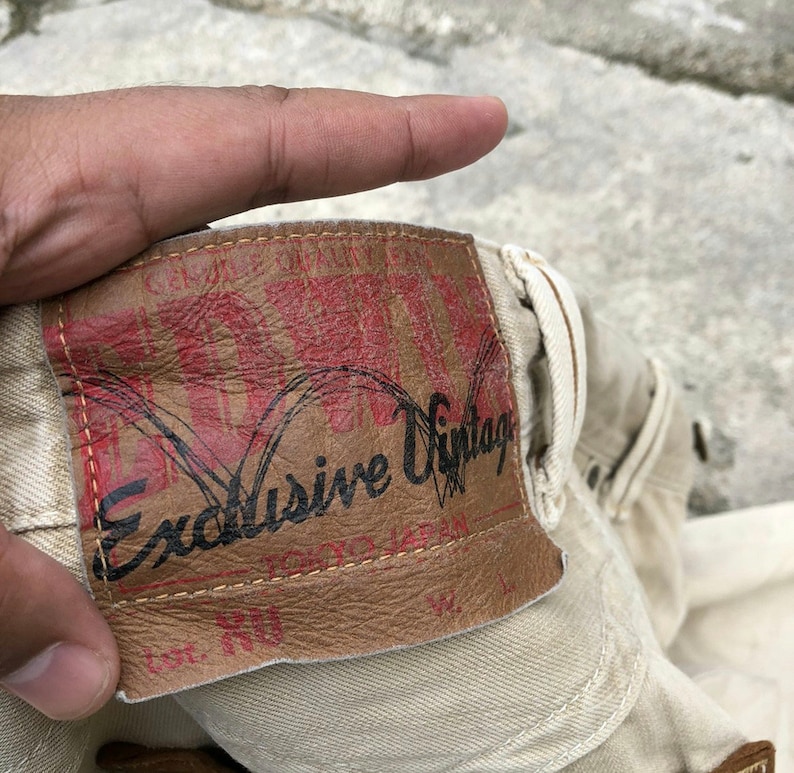 May include: Close-up of a beige denim fabric with a brown leather patch that says "Exclusive Vintage".