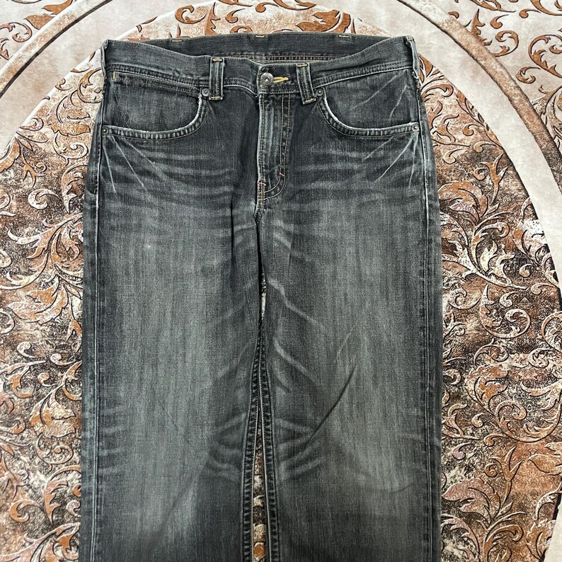 May include: A pair of faded black denim jeans. The jeans have a classic five-pocket design with a button and zipper closure. The fabric shows signs of wear and fading, with visible creases and subtle color variations.