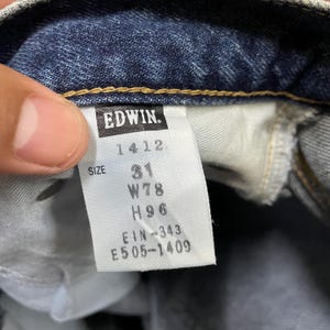 Puede incluir: Primer plano de una etiqueta de jeans de mezclilla con la marca "EDWIN". La etiqueta muestra la talla "31", la medida de la cintura "W78cm" y la medida de la cadera "H96cm". Los n&uacute;meros adicionales incluyen "1412", "EIN-343" y "E505-1409".