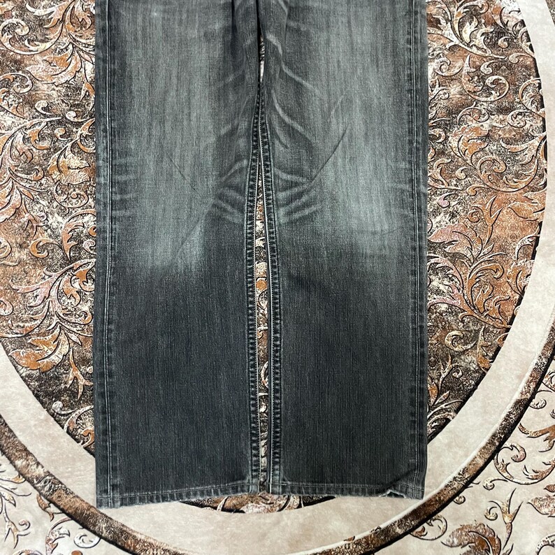 May include: Faded black denim jeans with a straight leg cut. The jeans have a classic five-pocket design and a button and zipper closure. The denim has a worn look with subtle fading and distressing.