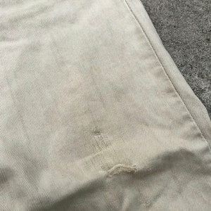 May include: A close-up of a light beige fabric with a small tear in the center.