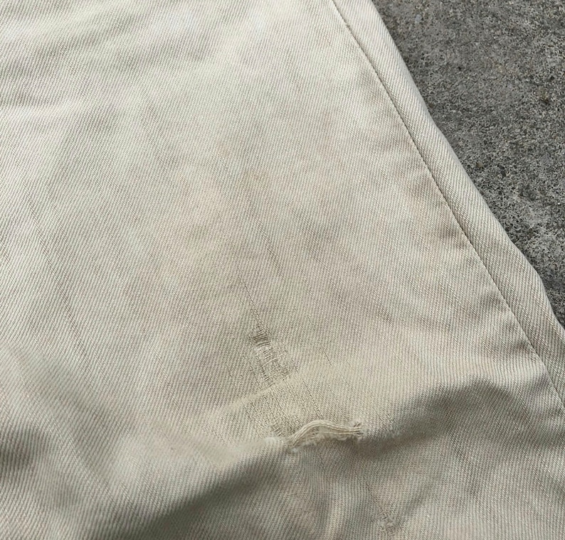 May include: A close-up of a light beige fabric with a small tear in the center.