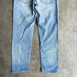 May include: Pale blue denim jeans with a faded wash. The jeans feature a classic five-pocket design and a straight leg fit. The back pockets and waistband are visible. The denim has a worn appearance.
