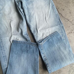 May include: Light blue denim jeans, folded and laid flat. The jeans have a faded wash and visible stitching details. The fabric appears worn, with a slight distressed look. The jeans are a classic style, suitable for casual wear.