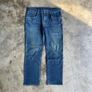 Op de afbeelding: Een spijkerbroek van blauwe denim met een klassiek ontwerp met vijf zakken. De jeans heeft een rechte pijp en een knoop- en ritssluiting. De denim heeft een vervaagde uitstraling, met lichtere plekken op de dijen en knie&euml;n.