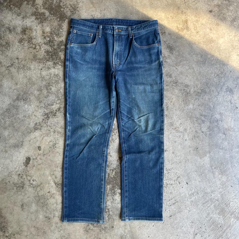 Op de afbeelding: Een spijkerbroek van blauwe denim met een klassiek ontwerp met vijf zakken. De jeans heeft een rechte pijp en een knoop- en ritssluiting. De denim heeft een vervaagde uitstraling, met lichtere plekken op de dijen en knie&euml;n.