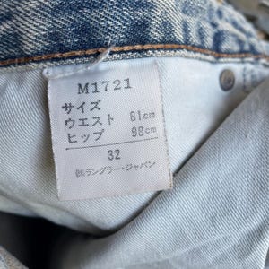 May include: Close-up of a light blue denim jeans label. The label displays the product code M1721, waist size 81cm, hip size 98cm, and size 32. The label also includes Japanese text.