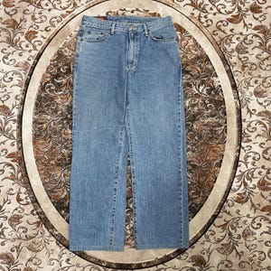 May include: Light blue denim jeans featuring a classic five-pocket design, a metal button closure, a zippered fly, and belt loops. The fabric displays a consistent medium wash with subtle fading along the thighs and seams, finished with stitching.
