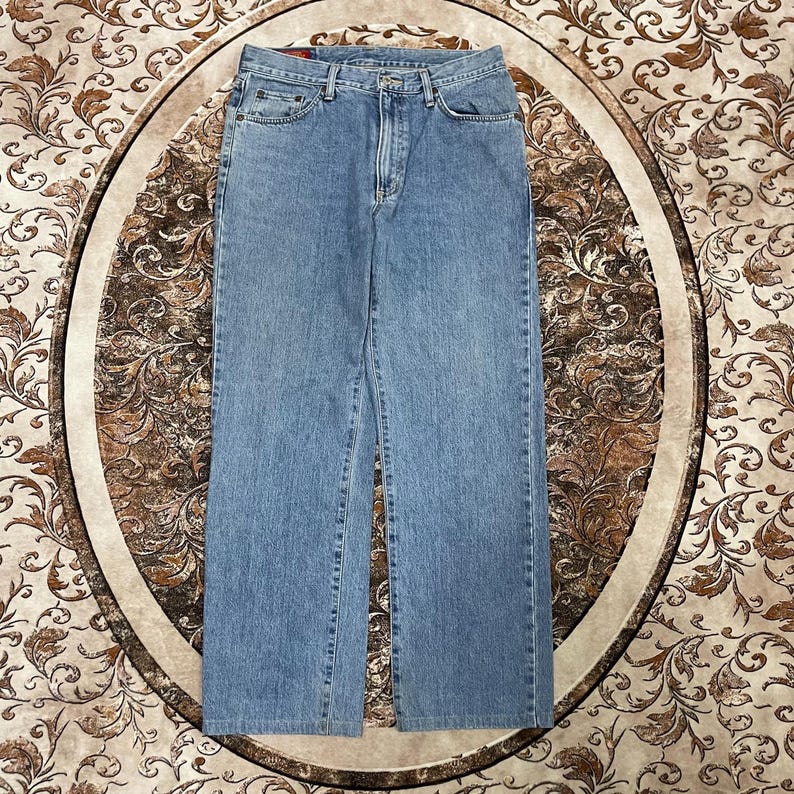 May include: Light blue denim jeans featuring a classic five-pocket design, a metal button closure, a zippered fly, and belt loops. The fabric displays a consistent medium wash with subtle fading along the thighs and seams, finished with stitching.