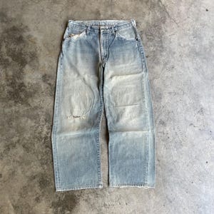May include: Light blue denim jeans with a faded wash and distressed details. The jeans have a relaxed fit, a button and zipper closure, and a ripped knee. The vintage-style jeans are a classic wardrobe staple.