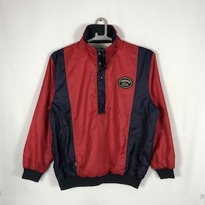 May include: A red and black windbreaker jacket with a Lacoste logo on the chest. The jacket has a high collar and a snap button closure.