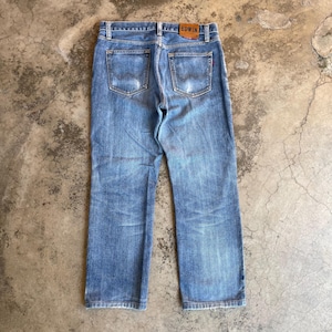 Pu&ograve; includere: Jeans in denim blu chiaro con lavaggio sbiadito e dettagli usurati. La vista posteriore mostra le tasche e una toppa in pelle marrone con il marchio "EDWIN". I jeans hanno un classico design a cinque tasche.