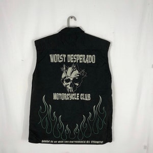 May include: Black sleeveless vest with a skull and flames graphic. The text "Worst Desperado Motorcycle Club" is printed on the vest. The text "Dance as if no one will catch you through all eternity!" is printed at the bottom.