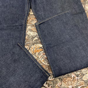May include: Close-up of dark blue denim jeans. The jeans have a classic five-pocket design with visible stitching in a contrasting yellow-tan color. The fabric appears to be a sturdy, durable denim.
