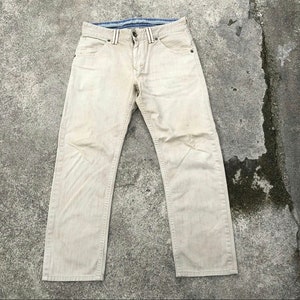 May include: A pair of light beige denim jeans with a straight leg fit. The jeans have a blue and white striped waistband.
