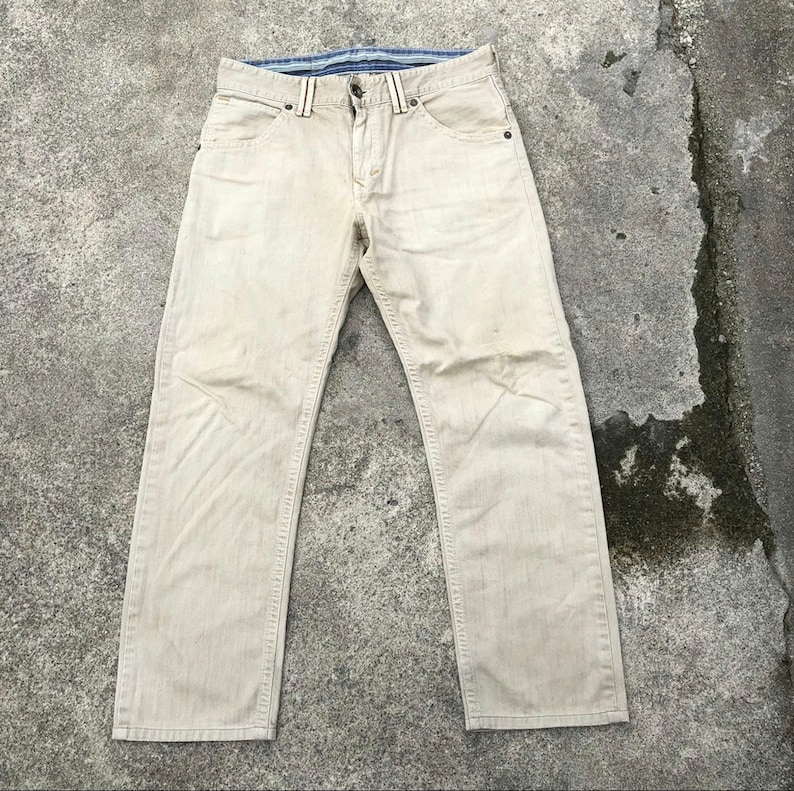 May include: A pair of light beige denim jeans with a straight leg fit. The jeans have a blue and white striped waistband.