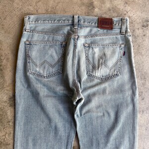 May include: Pale blue denim jeans with a classic five-pocket design. The back pockets have a distinctive W-shaped stitch. A brown leather patch with the brand name "EDWIN" is visible at the waistband. The jeans have a straight leg cut.