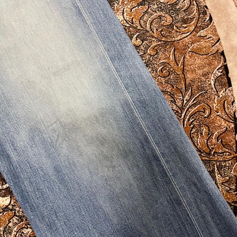 May include: Close-up of light blue denim jeans. The jeans have a faded appearance with a lighter wash in the center. A vertical seam runs down the side. The jeans are slightly wrinkled.