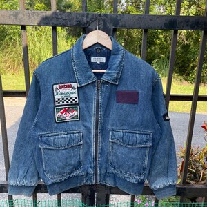May include: A blue denim jacket with a zipper closure and multiple patches. The patches feature racing themes and the text "Racing Mississippi Clipper" and "Racing Spirit".