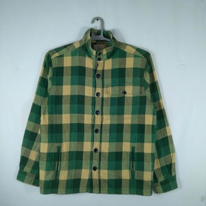May include: A green and tan plaid flannel shirt with a button-up front and a collar. The shirt has two pockets on the front.