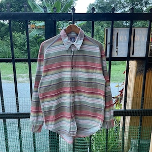 May include: A long-sleeve button-down shirt by Gap featuring a horizontal striped pattern in muted tones of red, green, tan, and white. The shirt includes a standard collar, a single chest pocket on the left side, and a full-length button placket.
