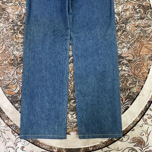 Puede incluir: Un par de vaqueros azules de mezclilla con un dise&ntilde;o de pierna ancha. Los vaqueros est&aacute;n hechos de tela de mezclilla de lavado medio y tienen un dise&ntilde;o cl&aacute;sico de cinco bolsillos. Los vaqueros est&aacute;n colocados planos sobre una superficie estampada.