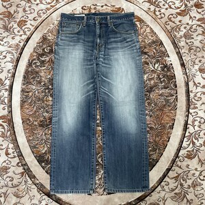 May include: A pair of blue denim jeans featuring a faded wash, a classic five-pocket design, a button fly closure, and visible stitching along the seams. The fabric displays a light blue centre with darker blue edges and a straight leg cut.