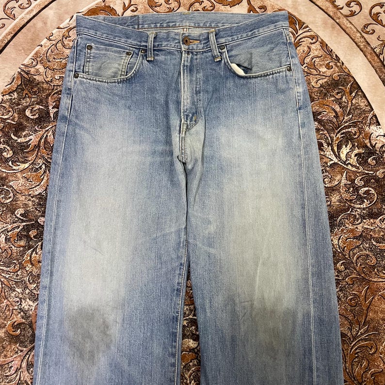 May include: Light blue denim jeans with a classic five-pocket design. The jeans have a faded wash and a straight leg cut. The front features a button closure and a zipper fly. The fabric appears to be a medium-weight denim.