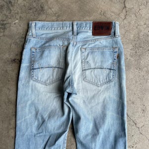 May include: Pale blue denim jeans with a traditional five-pocket layout. The rear pockets have decorative stitching. A brown leather patch with the brand name "EDWIN" is on the waistband.