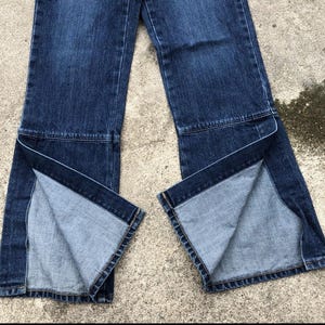 Op de afbeelding: Een paar donkerblauwe spijkerbroeken met een gesplitst beenontwerp. De jeans heeft een wijde beenopening en is gemaakt van een zachte, comfortabele stof.