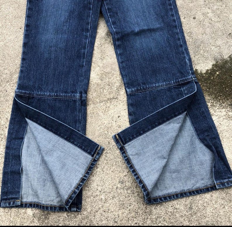 Op de afbeelding: Een paar donkerblauwe spijkerbroeken met een gesplitst beenontwerp. De jeans heeft een wijde beenopening en is gemaakt van een zachte, comfortabele stof.