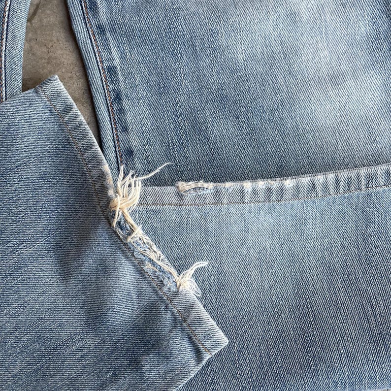 May include: Close-up of light blue denim jeans. The hem of the jeans is frayed, with visible threads and a distressed appearance. The fabric shows a classic denim texture.