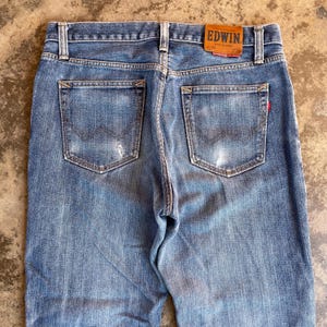 Pu&ograve; includere: Jeans in denim blu sbiadito con due tasche posteriori e una toppa in pelle. I jeans hanno un classico design a cinque tasche e una vestibilit&agrave; dritta. L'etichetta del marchio Edwin &egrave; visibile sul retro.
