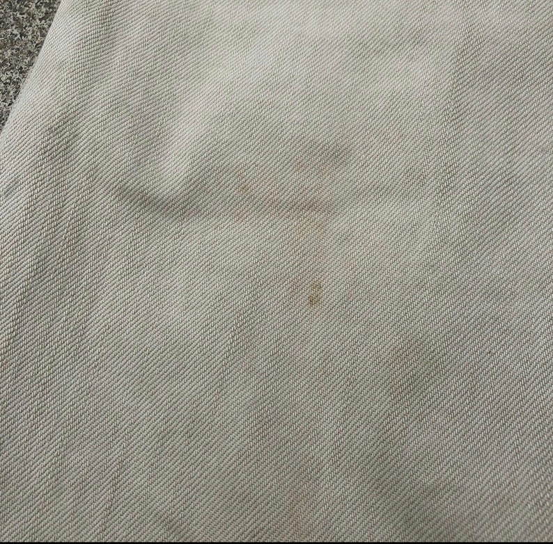 May include: A close-up of a light beige fabric with a subtle woven texture. The fabric has a slight discoloration in the center.