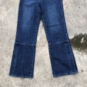 Op de afbeelding: Een paar donkerblauwe spijkerbroeken met een wijde pijp en een uitlopende zoom. De broek heeft een naad aan de voorkant van elk been en een naad aan de achterkant van elk been.