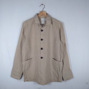 May include: A beige linen jacket with a button-up front and two patch pockets. The jacket has a collar and long sleeves.