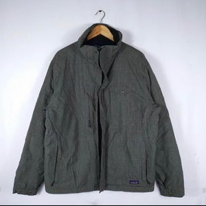May include: A grey and black patterned jacket with a zip and snap closure. The jacket has a high collar and two pockets on the front. The Patagonia logo is visible on the bottom right side of the jacket.