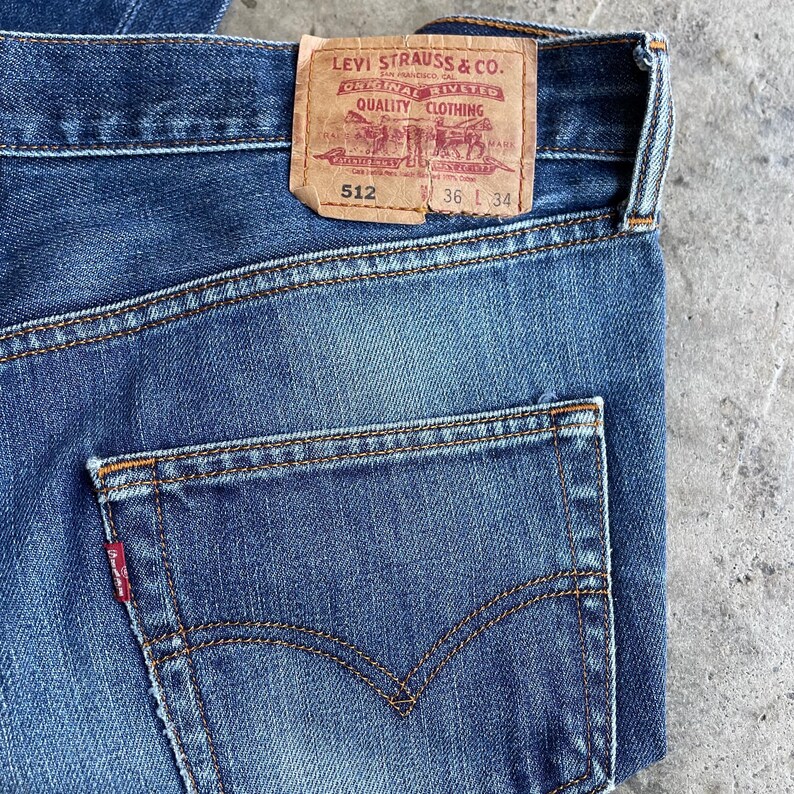 May include: Close-up of blue denim jeans with a faded wash. The back pocket is visible, along with the Levi Strauss & Co. label. The label reads "512" and "36 L 34".