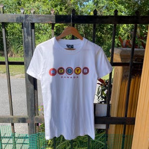 Camiseta vintage de los 90 con diseño de raíces canadienses multicolor en el centro, con burbujas y estampado de raíces canadienses, color blanco, talla pequeña.
