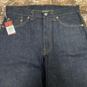 May include: Dark wash denim jeans with a classic five-pocket design. The jeans feature yellow stitching, copper rivets, and a button closure. A red tag with the brand name "JOE" is attached to the front pocket.