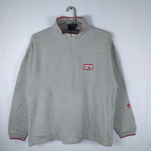 May include: A gray long-sleeve sweatshirt with a red and white logo that says "Hang Ten" on the front. The sweatshirt has a quarter-zip closure and red trim around the collar and cuffs.