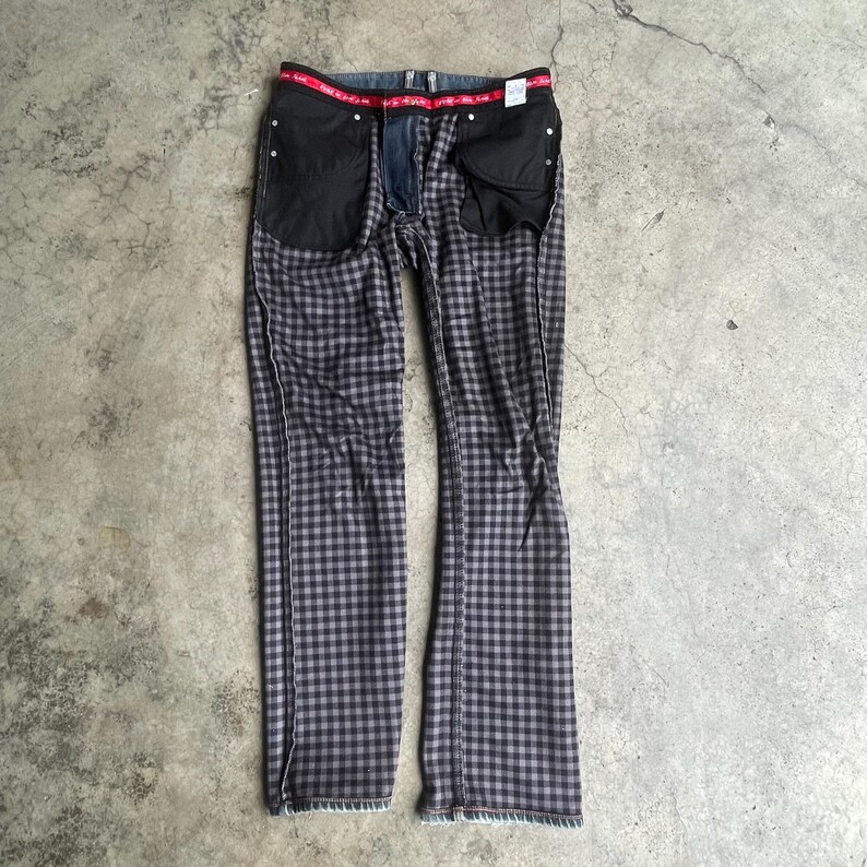 K&ouml;nnte beinhalten: Eine Jeanshose mit grau-schwarzem Karomuster und rotem Bund. Die Jeans liegt flach, wodurch die Innentaschen und der Rei&szlig;verschluss sichtbar werden. Der Stoff hat ein ausgepr&auml;gtes Karomuster.