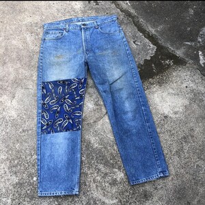 Puede incluir: Vaqueros de mezclilla azul con un parche de tela con estampado paisley en la rodilla izquierda.